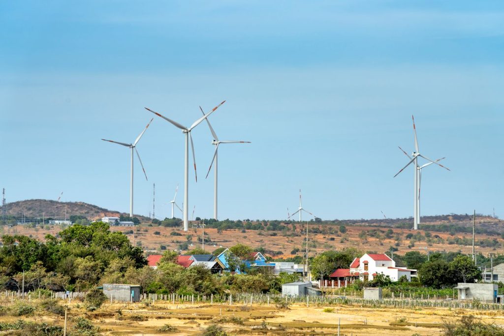 windmills-on-highland-between-countryside-houses-under-cloudy-sky-6416349 Scenic view of wind generators on land between buildings and mount under cloudy blue sky